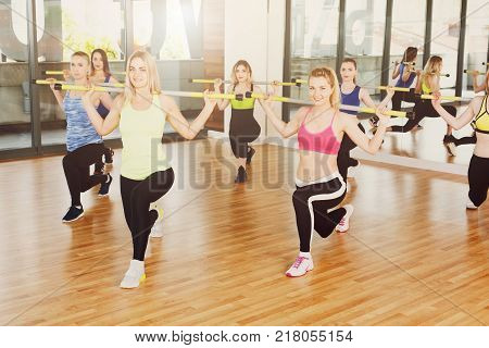 Group of young women in fitness class. People making exercises. Girls do lunges with barbells. Healthy lifestyle, intensive fitness training