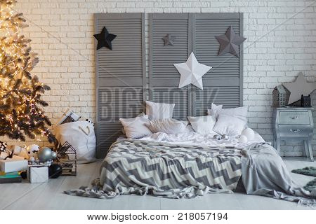 The bedroom decorated for Christmas. Cozy gray home interior. New year decoration. bright bedroom room with large double bed. Christmas tree with shyning garland