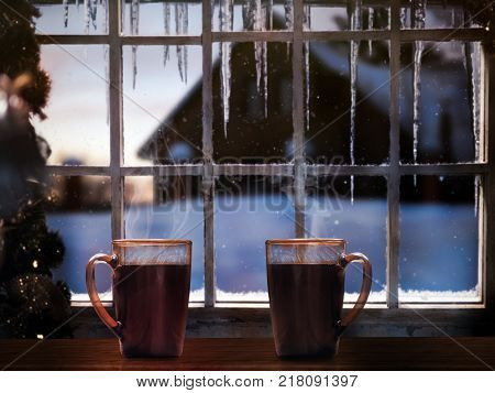 Two mugs with coffee on a background of a winter window. Snow falling icicles. Christmas tree