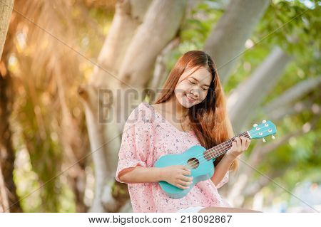 asian lady with hat play ukulele bossanova music in summer time.Young cute woman playing music outdo