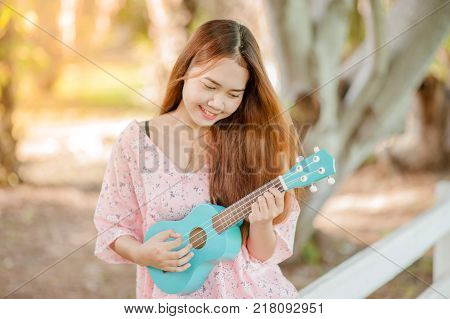 asian lady with hat play ukulele bossanova music in summer time.Young cute woman playing music outdo