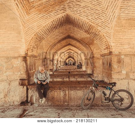 ISFAHAN, IRAN - OCT 14, 2014: Under famouse persian Pol-e Khaju bridge and elderly active man reading a book on October 14, 2014. The 3rd largest city of Iran Isfahan is an example of Islamic culture