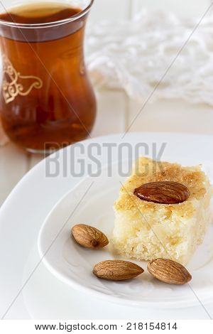 Piece Basbousa Traditional Arabic Semolina Cake with Nuts Orange Blossom Water and glass of tea. Selective focus.