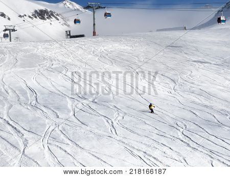 Skier downhill on snowy ski with trace from skis and snowboards and gondola lift at nice sun day. Georgia region Gudauri. Caucasus Mountains in winter.