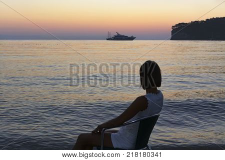 silhouette photo. young woman sitting on the beach and enjoying the sunrise. beautiful view of the bay. yacht in the background