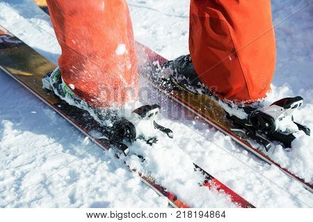 Orange alpine ski boots in a ski mount. One boot is completely fixed on skis, the second is not. Close-up. Orange suit