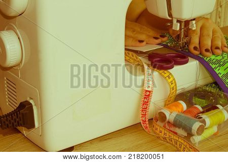 woman's hands using sewing machine with reels of colour threads. Workplace of tailor. people needlework and tailoring concept - tailor woman threading needle of sewing machine