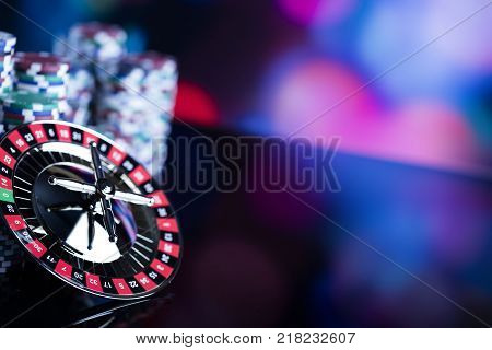 Casino theme. High contrast image of casino roulette and poker chips on a gaming table, all on colorful bokeh background. Place for typography and logo.