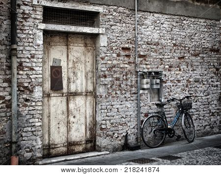 blue bike against an old painted white brick all and rusting metal door in italy
