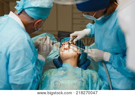 Male Old Professional Dentist Surgeon In Uniform And Female Assistant Helps To Performing Operation