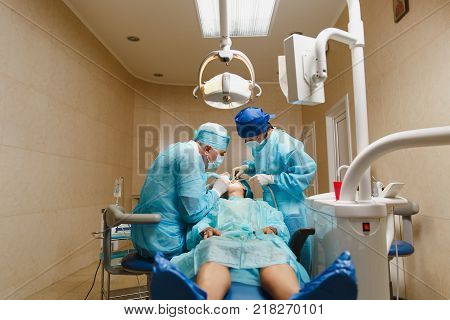Male Old Professional Dentist Surgeon In Uniform And Female Assistant Helps To Performing Operation