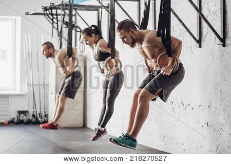 three attractive young male and female adults doing pull ups on rings