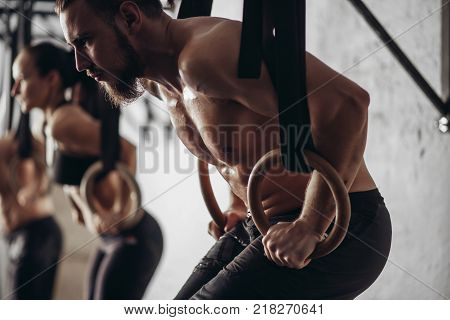 three attractive young male and female adults doing pull ups on rings