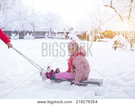 a small child on a sled. girl rolls on snowdrifts in winter sun shines