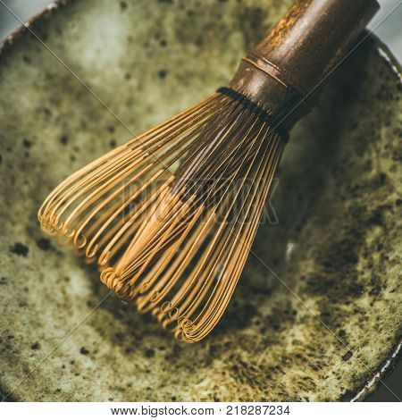 Flat-lay of Japanese tools for brewing matcha tea. Matcha powder in tin can, Chasen bamboo whisk, Chawan bowl over grey background, top view, square crop