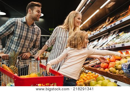 Happy family with child and shopping cart buying food at grocery store or supermark