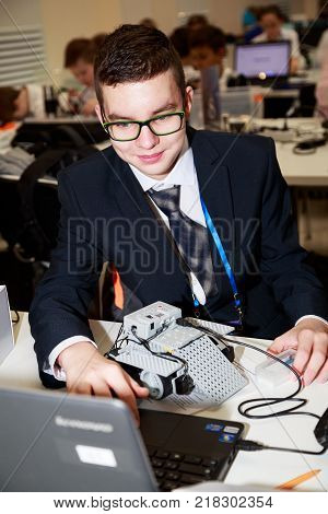 MOSCOW/ RUSSIA - DECEMBER 13, 2017. Smiling schoolboy with laptop, programming the robot at robotics competitions.