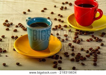 two coffee cups with diferent colors with coffee beans liyng in the background