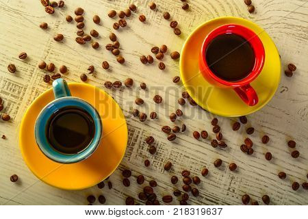 two coffee cups with diferent colors with coffee beans liyng in the background