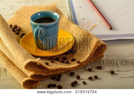 coffee cup with coffee beans liyng in the background with a book for taking notes on side