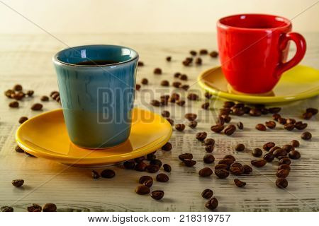 two coffee cups with diferent colors with coffee beans liyng in the background