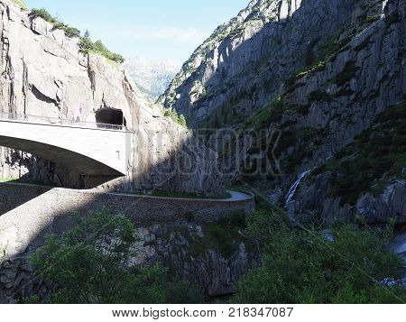 St. Gotthard and Teufelsbruecke, alpine Devil's road bridge and tunnel over Reuss river near Andermatt town in Switzerland, rocky mountains landscape scenery in 2017 warm summer day, Europe on July.