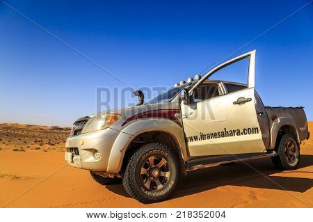 Merzouga Morocco - February 25 2016: Silver Toyota Hilux car with open front door and view to the desert. Merzouga is famous for its dunes the highest in Morocco.