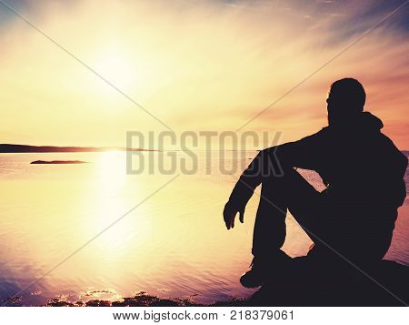 Lonely man hiker sits alone on the rocky coast and enjoying sunset. View over rocky cliff to free ocean