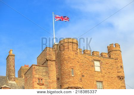 Close up of the tower of the Castle of Mey with british flag located on north coast of the Highlands in Scotland, United Kingdom on a blue sky.