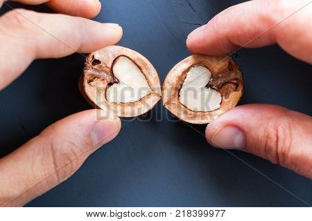 Two hands male and women are holding two halfs of walnut in shape of heart on dark wooden table. Top view.