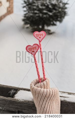 Still Life The love of two hearts warms in cold snow. Two pink hearts on the straw in the snow Inside the hearts written in red letters love and painted a small heart.