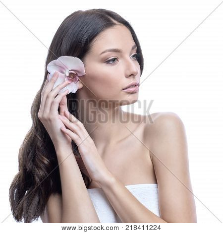 Young and healthy woman with light make-up on white background. The hair is decorated with beautiful fresh Orchid flower. SPA and skin care concept.