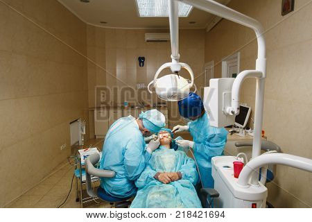 Male Old Professional Dentist Surgeon In Uniform And Female Assistant Helps To Performing Operation