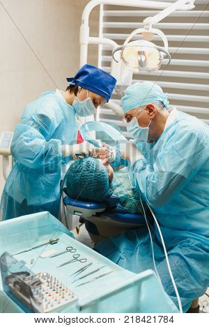 Male Old Professional Dentist Surgeon In Uniform And Female Assistant Helps To Performing Operation