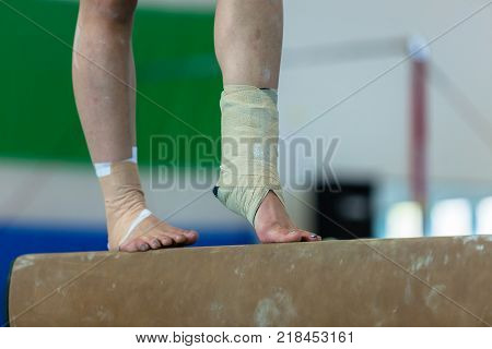 Gymnastics teenager girl closeup legs feet ankles bound with tape strapping from injuries on balance beam routine.
