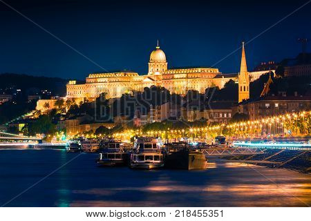Evening view of Buda Castle with city lights and ship on the Danube river. Colorful cityscape in Budapest Hungary Europe. Artistic style post processed photo.