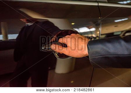 Male hand holding silver doorhandle a white car