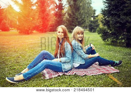 Girls Couple Are Sitting In The Sunny Park. Picnik