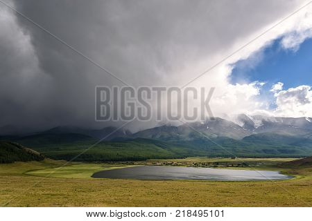 Scenic view with storm clouds over the plateau with a lake and mountains covered with snow and forest and part of a blue sky with sunlight