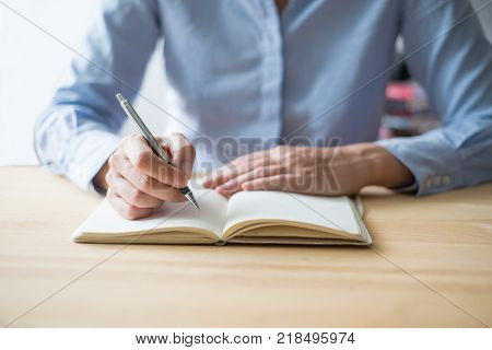 Cropped view of person writing in notebook and sitting at table. Front view.