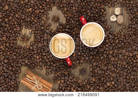 Two cups of coffee with a foam top view. Coffee beans badon cinnamon on a wooden surface with place for text. Love of a coffee drink. Morning invigorating coffee for two with copy space.