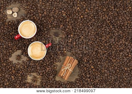 Two cups of coffee with a foam top view. Coffee beans badon cinnamon on a wooden surface with place for text. Love of a coffee drink. Morning invigorating coffee for two with copy space.