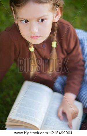 Adorable happy little preschooler girl with pigtails ready back to school reading textbooks outdoors school books manuals. Wearing school uniform. Warm september fall day. Smart clever intellegent little girl.