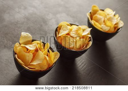 Three black bowls with crunchy potato chips on the table. Concept of unhealty snack food.