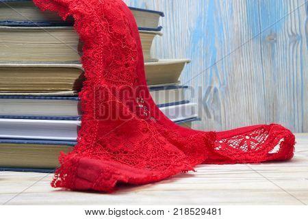 Red lace g- string and a pile of old books on the table in the university library. Red lingerie