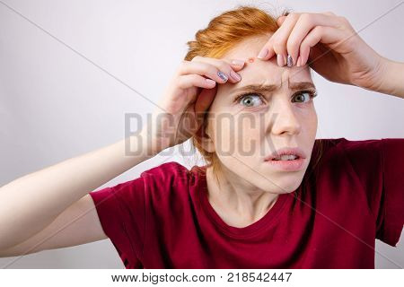 Young redhead woman squeezing her pimples, removing pimple from her face