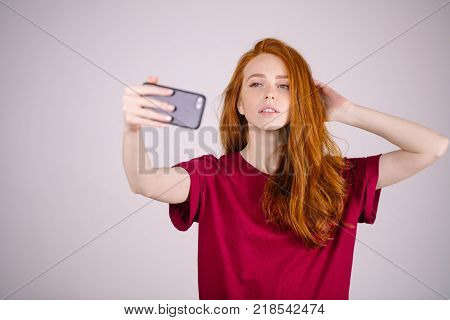 Cute redhead girl takes a selfie. She has long red hair. wears marsala t-shirt