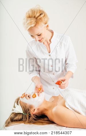 Beautiful young woman receiving fruit mask on a face in beauty salon - indoors.