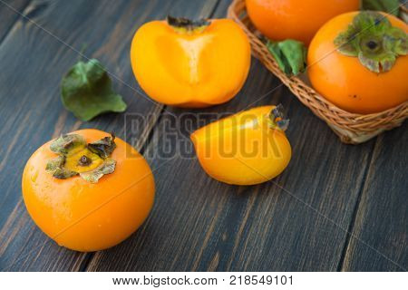 Sliced ripe persimmons with green leaves on dark rustic wooden background closeup