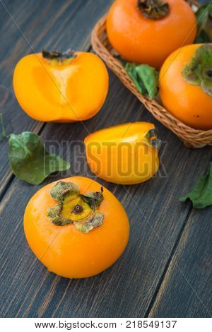 Sliced bright orange persimmons on black rustic wooden background closeup
